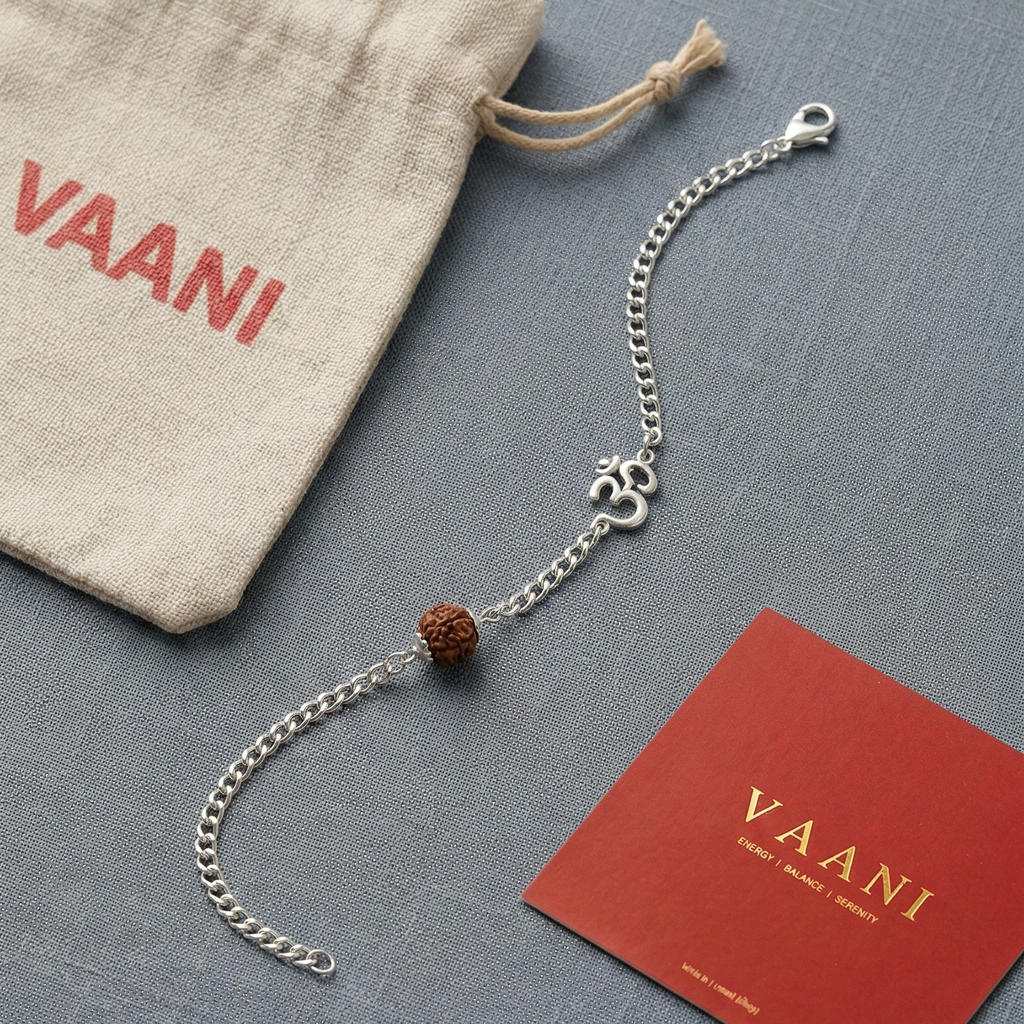 Silver bracelet with a red bead on a gray surface, next to a beige drawstring bag and a red card with 'VAANI' branding.