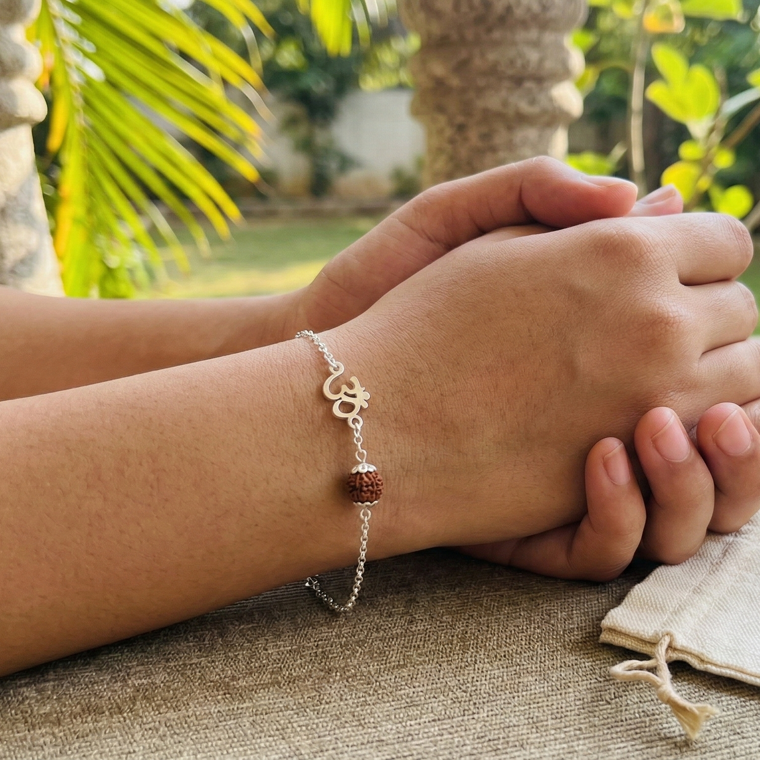 Person wearing a bracelet with a tag labeled 'Om Rudraksha' on a textured surface with greenery in the background.